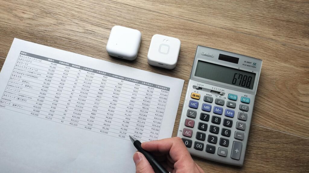 2つの子ども用GPSの料金表をノートに書き出し、金額差がほとんどないことを比較しているイメージ写真。