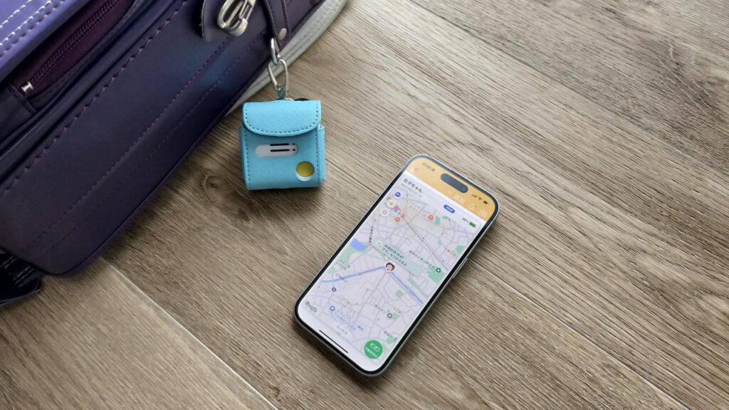 ランドセルの横に子ども用GPS端末と、位置情報が表示されたスマホを並べた写真。
