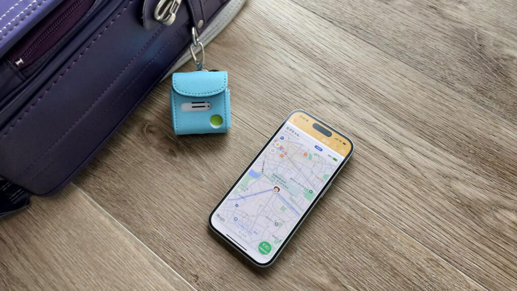 ランドセルの横に子ども用GPS端末と、位置情報が表示されたスマホを並べた写真。