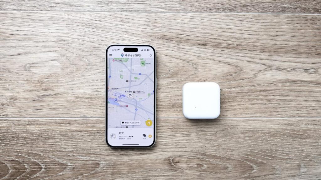 みまもりGPSの端末本体と、シンプルな地図画面を表示したスマホを並べた写真。